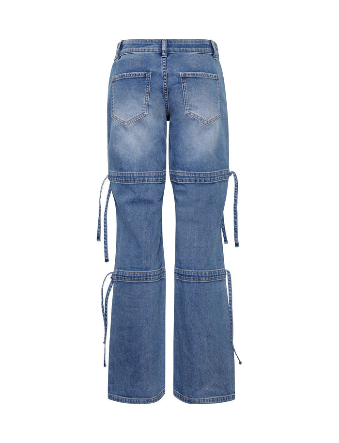A pair of light wash blue BAINES PANTS from TIGERMIST is seen from the back. The pants feature two back pockets, two additional knee pockets, and extended seams around the knees with tie details. With a slightly faded look and a wide-leg cut, these jeans blend style and practicality seamlessly.