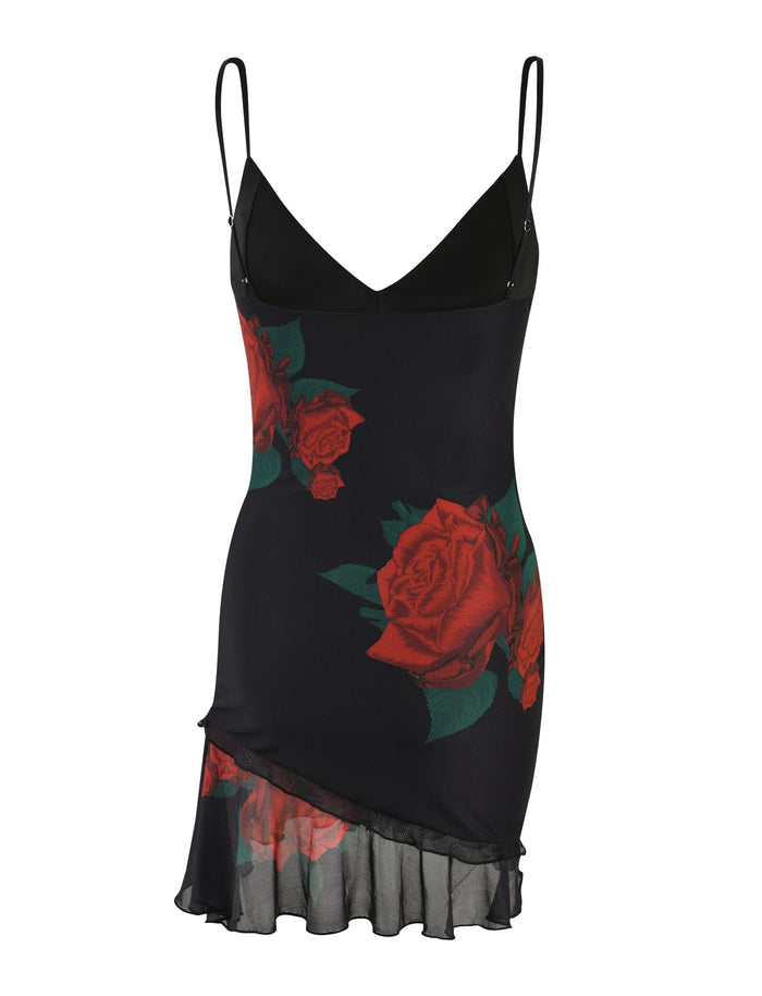 The CARLY DRESS - BLACK: MACRO ROSE- RED ROSE by TIGERMIST is a sleeveless slip dress adorned with large red rose prints. It features thin spaghetti straps, a deep V-neckline, and a layered asymmetrical hem with a sheer ruffle trim, accentuating its elegant and romantic design.