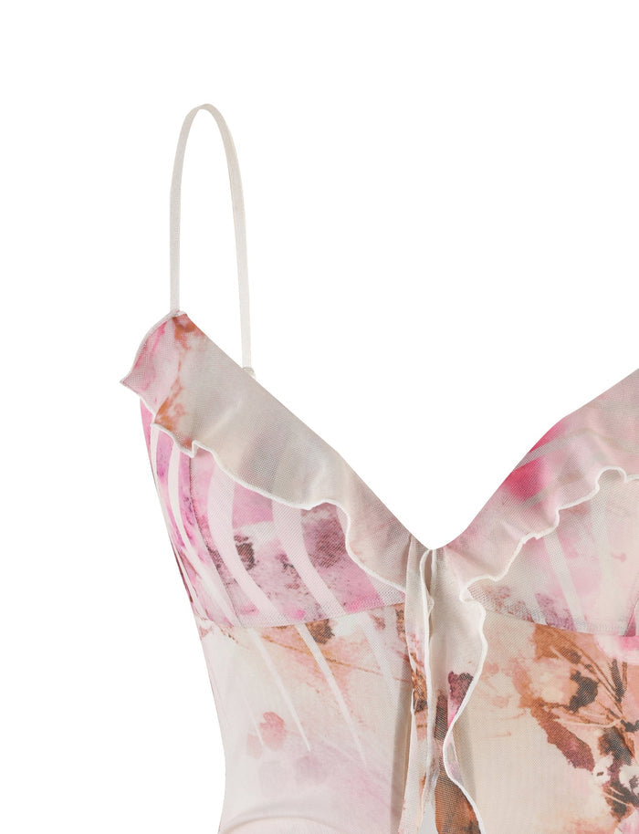 A close-up image of the Tigermist Carly Dress - Multi : Floral, showcasing its spaghetti strap design and soft pastel abstract pattern. The fabric exhibits a light pink and beige watercolor effect with subtle hints of other colors. The dress features ruffled detailing along the neckline and a small bow around the bust area.