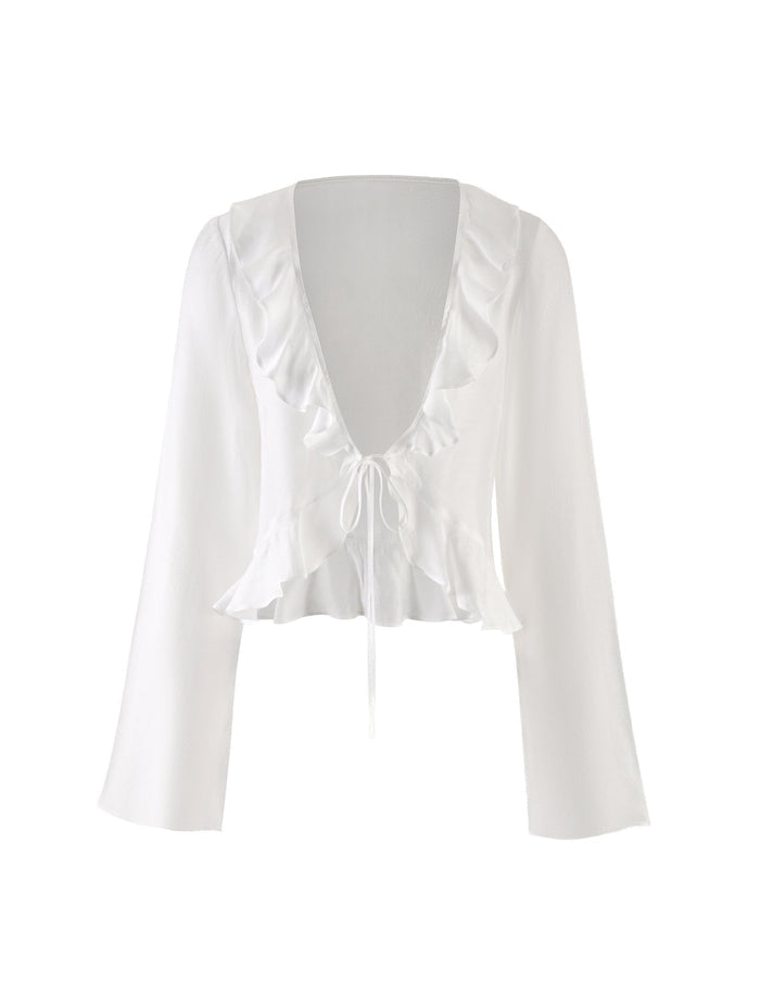The CORVIN TOP - WHITE by TIGERMIST is a stylish white long-sleeve crop top featuring a deep V-neckline adorned with ruffled trim around the neckline and waist. It ties together at the center with a string bow, while the slightly flared sleeves add an elegant touch to this garment.