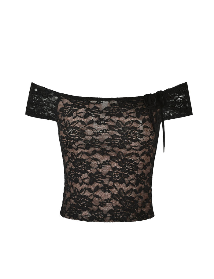 This image showcases the CYD TOP - BLACK from TIGERMIST, featuring an off-the-shoulder design with a floral lace pattern. The top also sports a small bow on one side of the neckline. The fabric appears to be sheer with a nude lining underneath the lace, complemented by short sleeves and a fitted design.