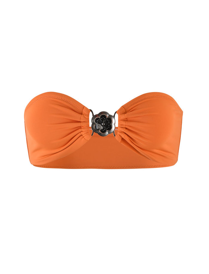 The CYNTHIA BIKINI TOP - BURNT ORANGE by TIGERMIST is a strapless top that features a ruched center with a decorative silver flower clasp. The fabric is smooth, and the design is simple and elegant.