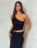 A person with long brown hair wears a stylish DEANNA TOP - BLACK from TIGERMIST and a matching black skirt. They pose with their hands resting on their hips against a light textured background.