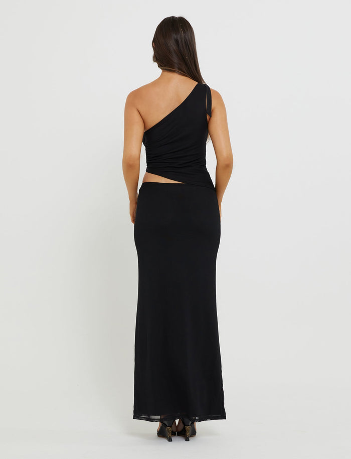 A person with long dark hair is standing with their back to the camera, showcasing a stunning Tiger Mist DEANNA TOP - BLACK paired with form-fitting pants and strappy black heels. The background is plain and white.