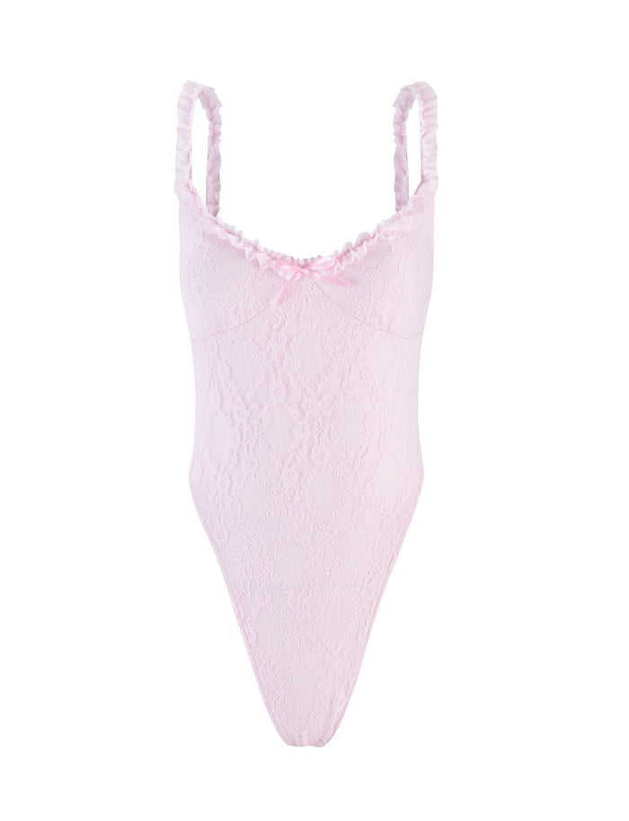 The DEJA BODYSUIT - PASTEL PINK by TIGERMIST features thin ruffled shoulder straps, a small satin bow at the center of the neckline, scalloped trim at the bust, and a high-cut leg design. The pink lace bodysuit showcases a delicate floral pattern for an intricate and delicate appearance.