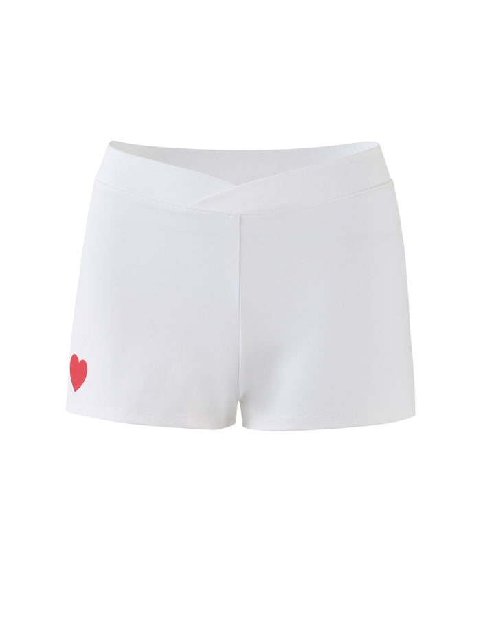 The DELANEY SHORT - WHITE by TIGERMIST are white athletic shorts that feature a high waistband and a small red heart graphic on the lower left side. The fabric is stretchy, and the design is simple and stylish.