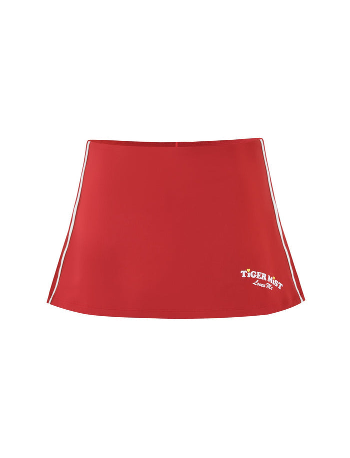The DELANEY SKORT - RED by TIGERMIST is a stylish red mini skort featuring a white embroidered "TIGER MIST Love Me" logo on the bottom right. Its sporty white side stripes make it perfect for casual wear, combining simplicity with fashion.