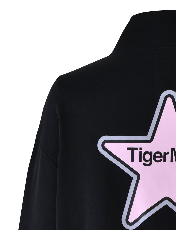 Close-up of the back of the DELFINA JUMPER - BLACK from TIGERMIST, featuring a large pink star with a grey outline. Inside the star, "TigerMode" is printed in bold black letters, echoing the iconic Tiger Mist style. The smooth fabric and high collar add to its sleek appearance.