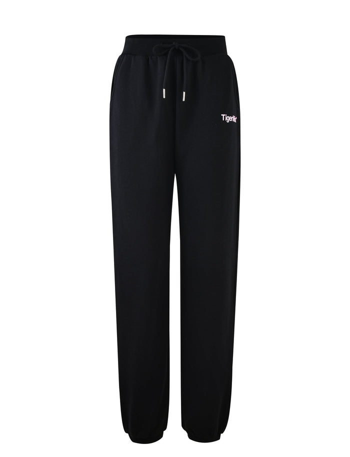 A pair of TIGERMIST DELFINA PANT in black featuring an elastic waistband, drawstrings, and cuffed ankles. There is a small logo that reads "Tigerle" in white and pink text on the left hip area.