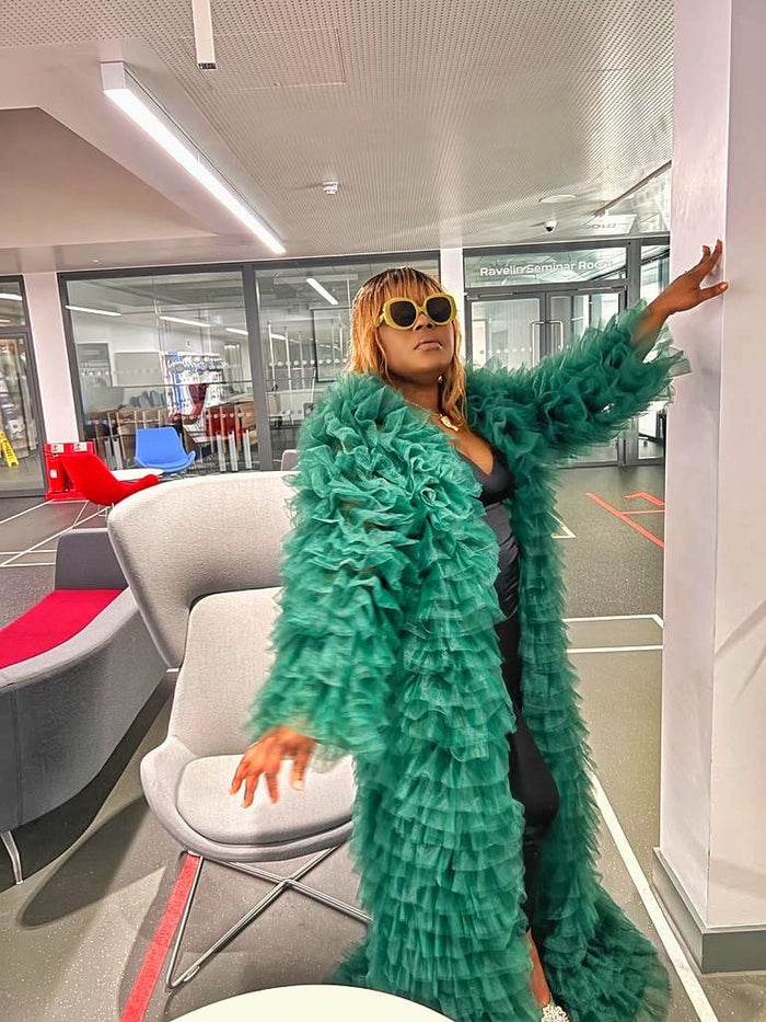 Side view of emerald tiered tulle statement coat styled over black outfit with layered volume
