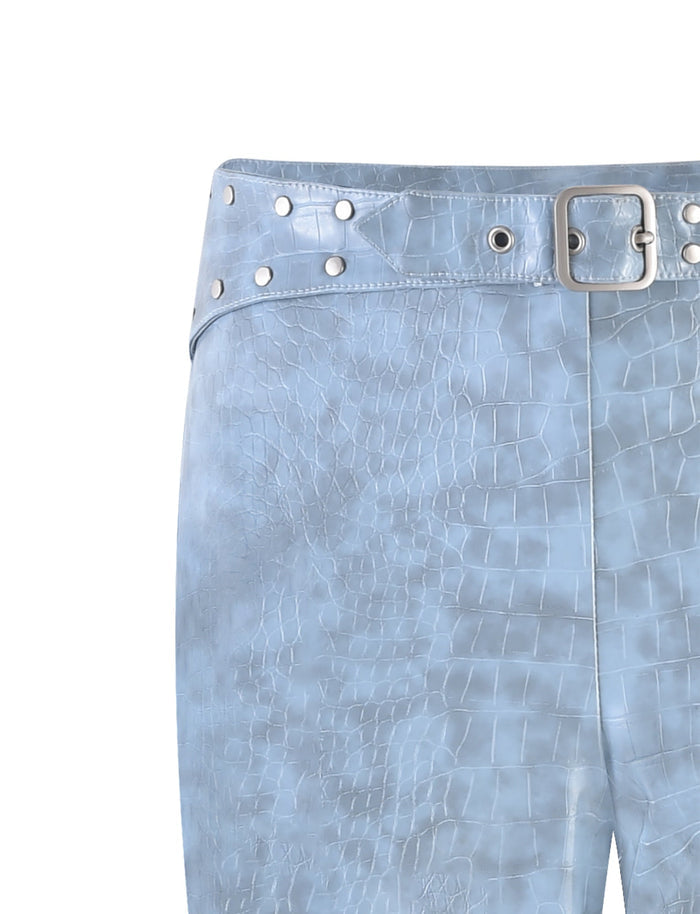 Close-up shot of the EMERSYN PANT - BLUE in Dusty Blue, featuring a crocodile-patterned design with a leather-like texture. These trendy pants, designed by TIGERMIST, boast a silver buckle and multiple silver studs at the waistband, showcasing their detailed texture and fashionable appeal.