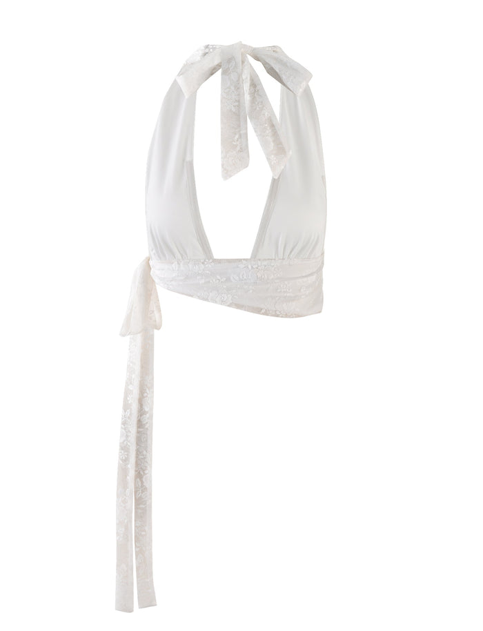 The Florian Top in white lace from Tigermist features a deep V-neck and delicate lace detailing. This high-stretch halter design ties around the neck and wraps around the torso, finishing with a long lace ribbon at the back. The crop length adds a modern twist to its feminine, slightly sheen fabric.