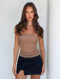 A woman with long, wavy brown hair is posing against a plain, light-colored background. She is wearing a Tiger Mist HARRIETT TUBE TOP in tan and a black mini skirt with a front slit, standing confidently while looking directly at the camera.
