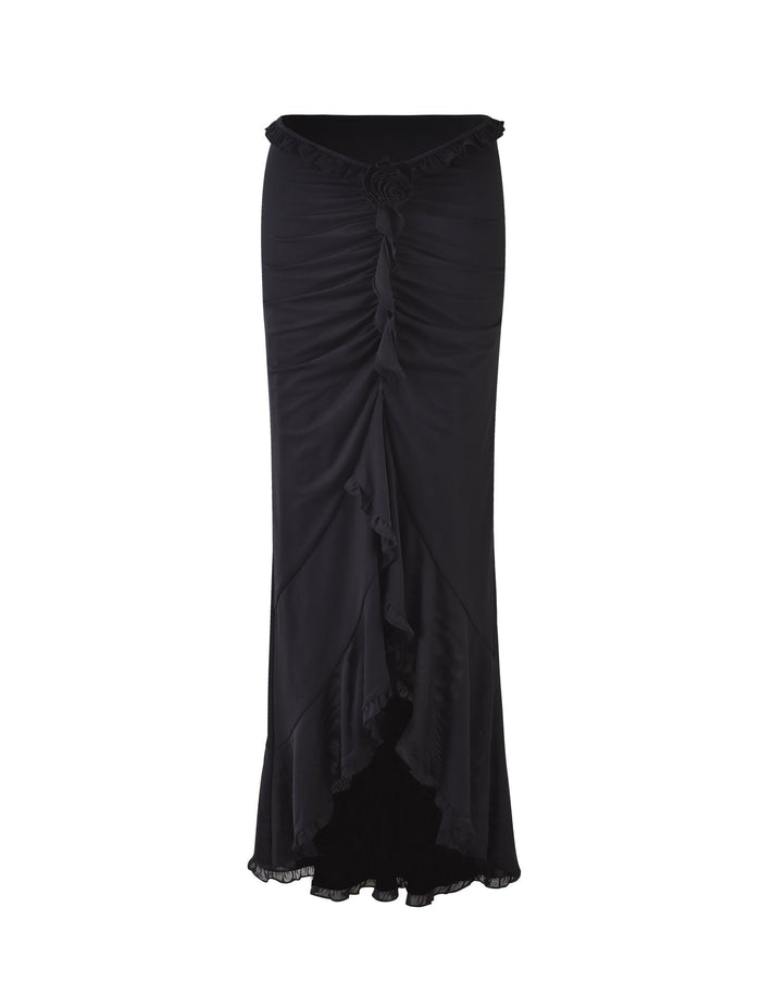 The HEAVEN MAXI SKIRT - BLACK by TIGERMIST is a high-waisted, ankle-length skirt with ruching along the front and a ruffled high-low hem. The fabric drapes in cascading folds, creating a flowing and elegant appearance. This skirt also features a decorative rosette at the center of the waistline.