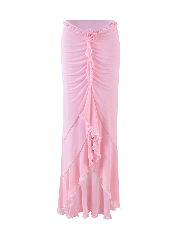 The HEAVEN MAXI SKIRT - PINK by TIGERMIST is a high-waisted, ankle-length skirt featuring a gathered design down the front and a decorative rosette at the waist. The hemline includes a ruffled edge, adding an elegant touch to its flowy fabric.