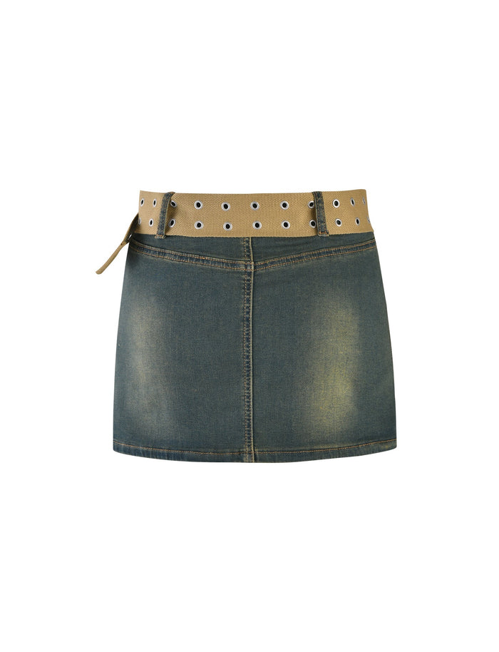 The ISABEL SKORT - BLUE from TIGERMIST is a high-waisted denim mini skirt featuring a light brown, grommet-studded belt. The skirt boasts a slight faded design on the front and lies flat against a plain white background.