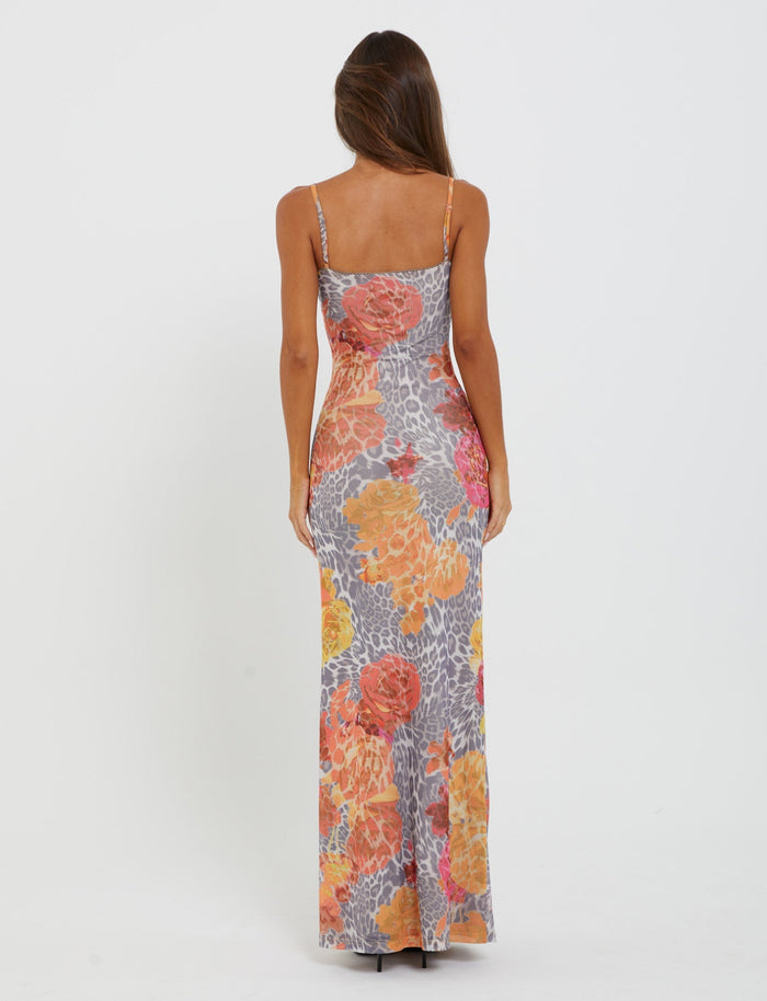 With their back to the camera, a person with long brown hair wears the JULIANNA DRESS from TIGERMIST, a floor-length, form-fitting dress adorned with thin straps and a vibrant orange leopard pattern.