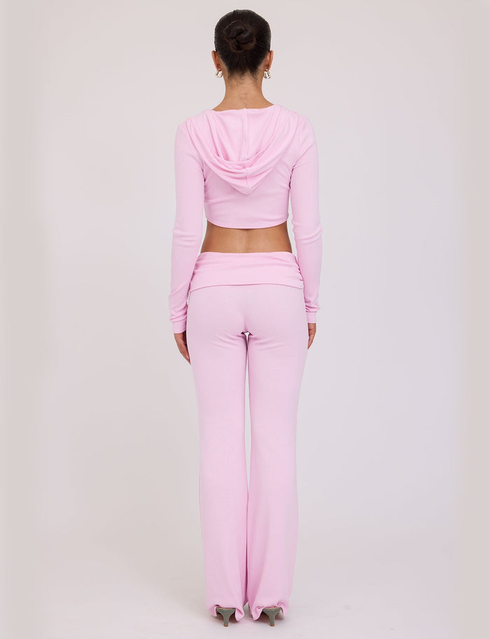 A person with hair in a bun is standing with their back to the camera, wearing a light pink TIGERMIST KARINA JUMPER and matching high-waisted, flared pants. The background is plain white.