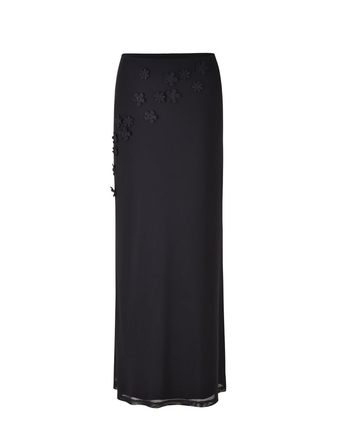 The KATINA SKIRT - BLACK by TIGERMIST is a long, elegant skirt featuring subtle, small floral embellishments scattered on the upper portion. Designed with a straight cut that reaches the ankles, it also boasts a slightly sheer hemline.