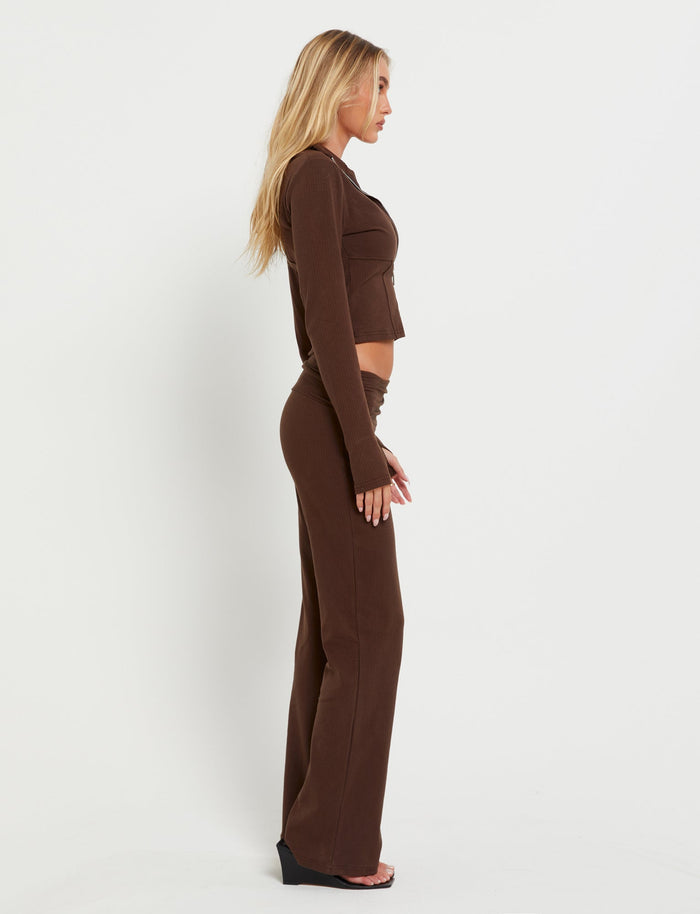 A woman with long, blonde hair stands in profile against a white background, wearing the KAVAT JACKET - BROWN from TIGERMIST. She appears to be posing, with her arms relaxed at her sides.