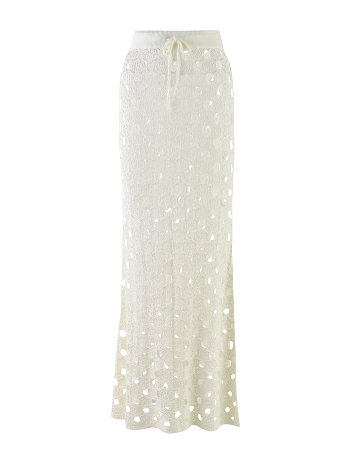 The Kincade Skirt by TIGERMIST is a long, white crochet skirt featuring a drawstring waist. Its intricate crochet pattern consists of hexagonal shapes that create a see-through design. The skirt falls gracefully to the floor, showcasing its elegant and airy style.