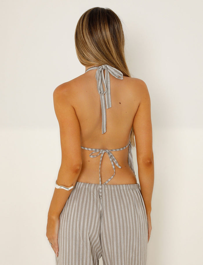 A woman with long hair, styled in a chic TIGERMIST outfit, is facing away from the camera, wearing a backless LAINEY TOP - GREY : STRIPE and matching striped pants. She has a bracelet on her right arm, and the background is plain white.