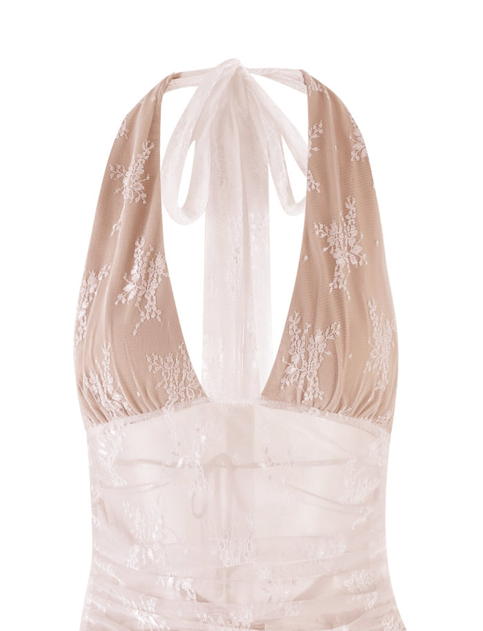 A close-up of the LENORA LACE DRESS - WHITE from TIGERMIST showcases its halter neckline and intricate floral lace patterns on a sheer fabric. The back ties into a bow at the neck, adding a delicate and elegant touch to the overall design.