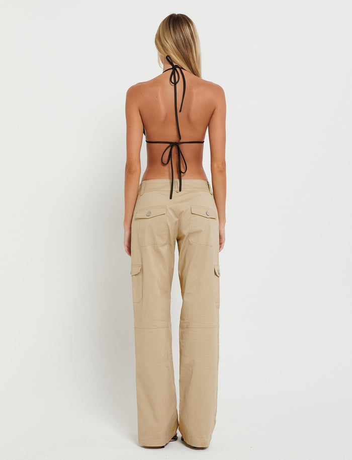 A person with long blonde hair is shown from the back, wearing a black halter bikini top and the LISSA PANT - NEUTRAL : BEIGE by TIGERMIST. The image is set against a plain white background.