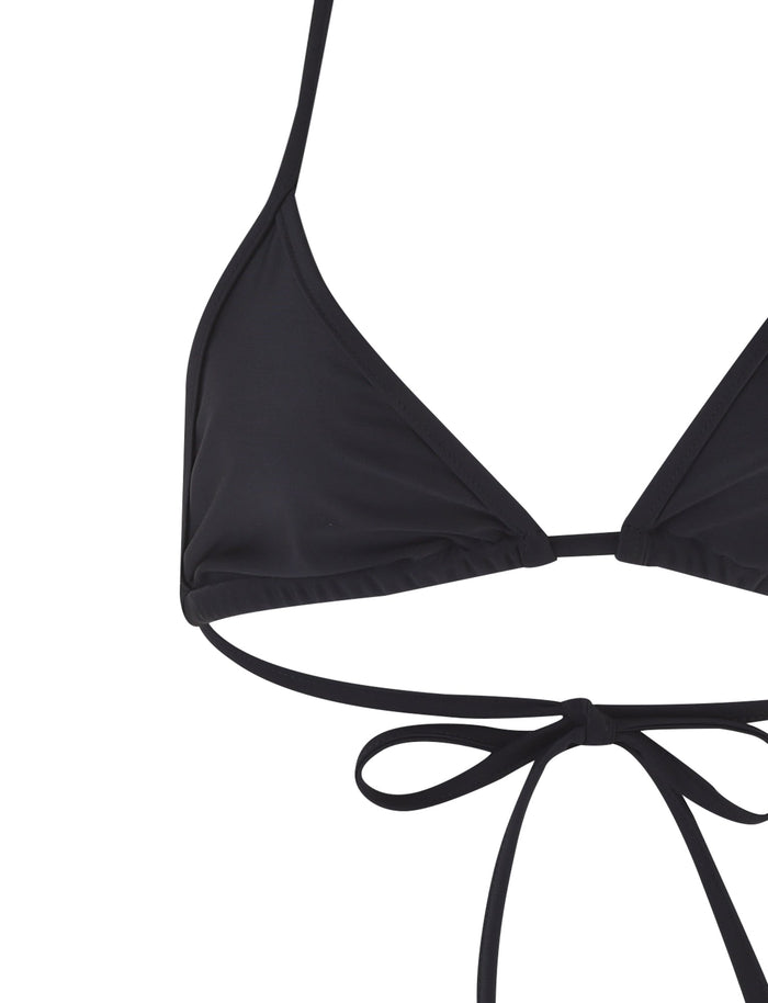 A close-up of the LULA BIKINI TOP - BLACK from TIGERMIST. The image captures the triangular cup on the left side along with its bottom ties. The string that ties around the neck and back is clearly visible, displaying the bikini top's smooth fabric.