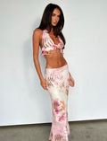 A person with long dark hair stands against a plain white background, wearing a TIGERMIST sleeveless, midriff-baring top and the MACEY SKIRT - MULTI : FLORAL. The outfit features a pink and white floral pattern, with a ruffled hem on the top and a high-waisted, form-fitting design on the skirt.