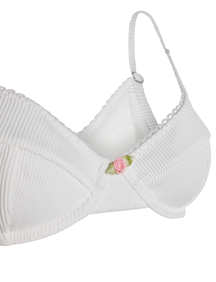 The MILANA BIKINI TOP - WHITE by TIGERMIST is a white ribbed swim top with adjustable straps, a pink rose at the center front, and a soft, seamless design for comfort without visible fasteners.