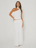 A woman stands against a plain background, wearing the stylish MIST SKIRT - WHITE from TIGERMIST. The skirt showcases an elegant wrap design with draped fabric, paired perfectly to highlight its chic one-shoulder style. She poses with one hand on her hip and the other resting by her side.