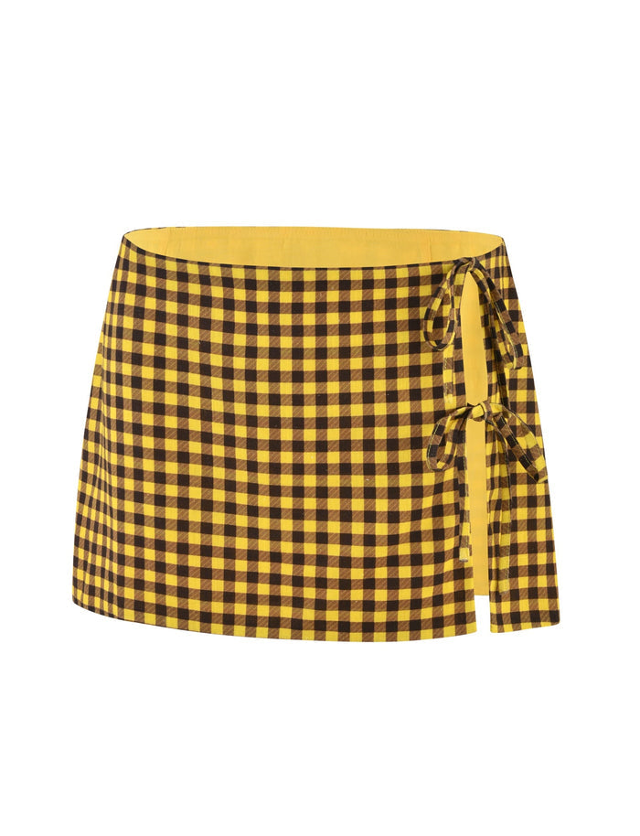 The NICOLA SKIRT - YELLOW : CHECK from TIGERMIST boasts a chic tie detail on the right side and features a vibrant, modern pattern of alternating yellow and black checkered squares.