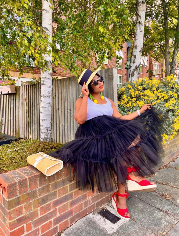 Woman in a black tulle skirt and red sandals sitting on a brick wall outdoors.