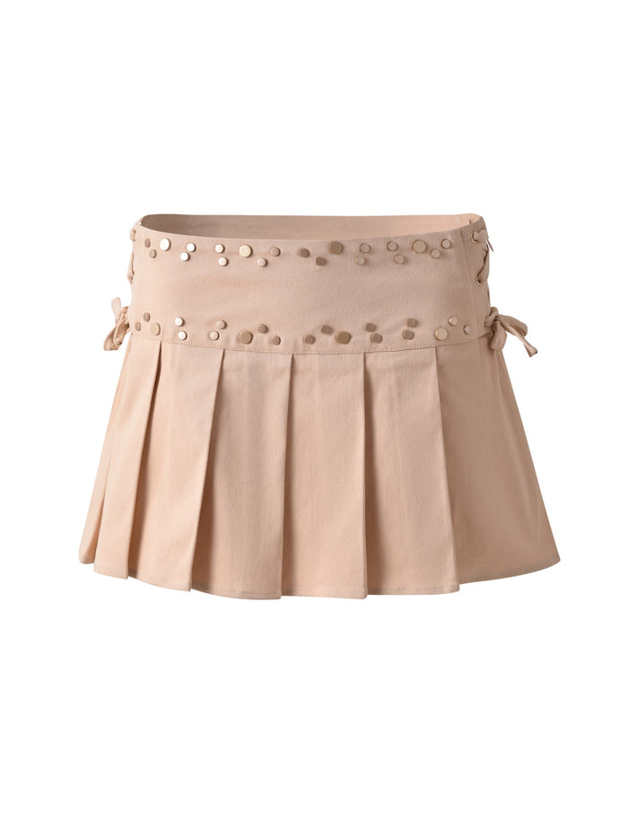 The NOVALIE SKIRT - BEIGE : TAN by TIGERMIST is a beige mini skirt with pleats and decorative circular studs around the waistband. It features side ties for added detail and is displayed on a plain white background.