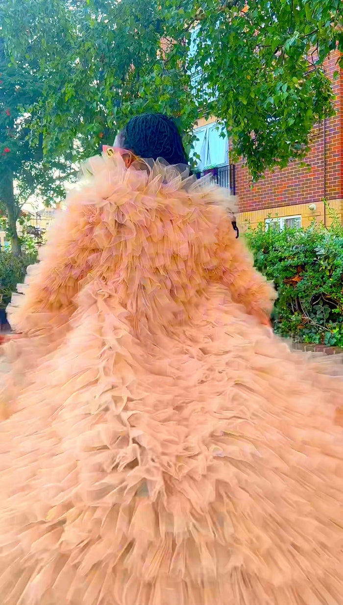 Person wearing a large, fluffy beige coat with a tree and building in the background