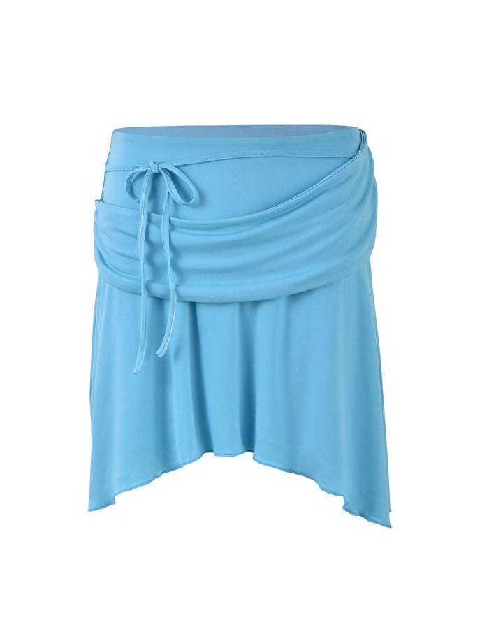 The PEARL SKIRT by TIGERMIST in bright sky blue is an asymmetrical piece with a ruched design and a tie detail at the waist. It features a flowing, draped appearance and a handkerchief hemline, providing a casual and relaxed look.