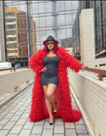 Woman wearing a red fur coat and black dress on a rooftop with cityscape background