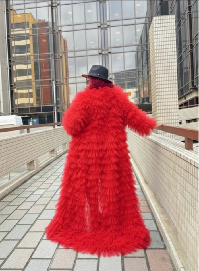 Person wearing a long red luxury tulle coat walking on a rooftop with cityscape background