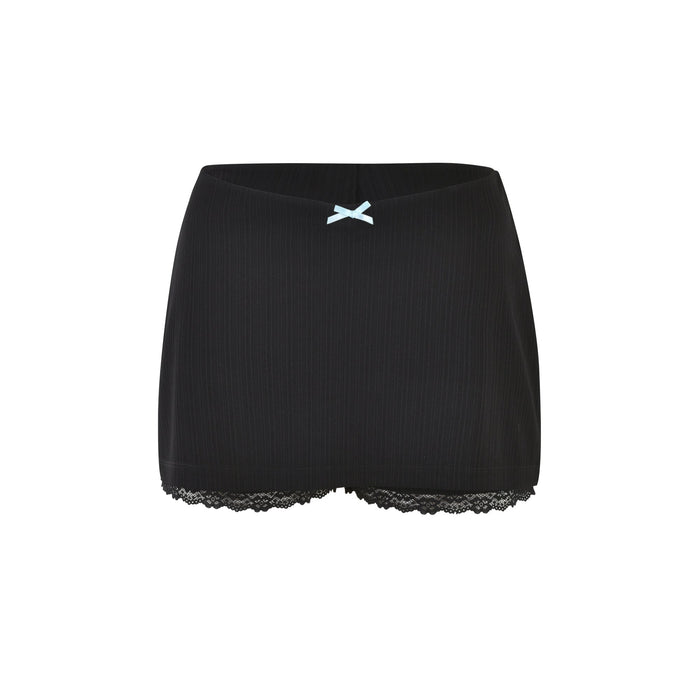 A pair of SABINE SKORT shorts in black from TIGERMIST featuring a vertical ribbed texture, a small light blue bow at the center of the waistband, and black lace trim at the leg openings. The skorts appear to be made of a soft, stretchy fabric.