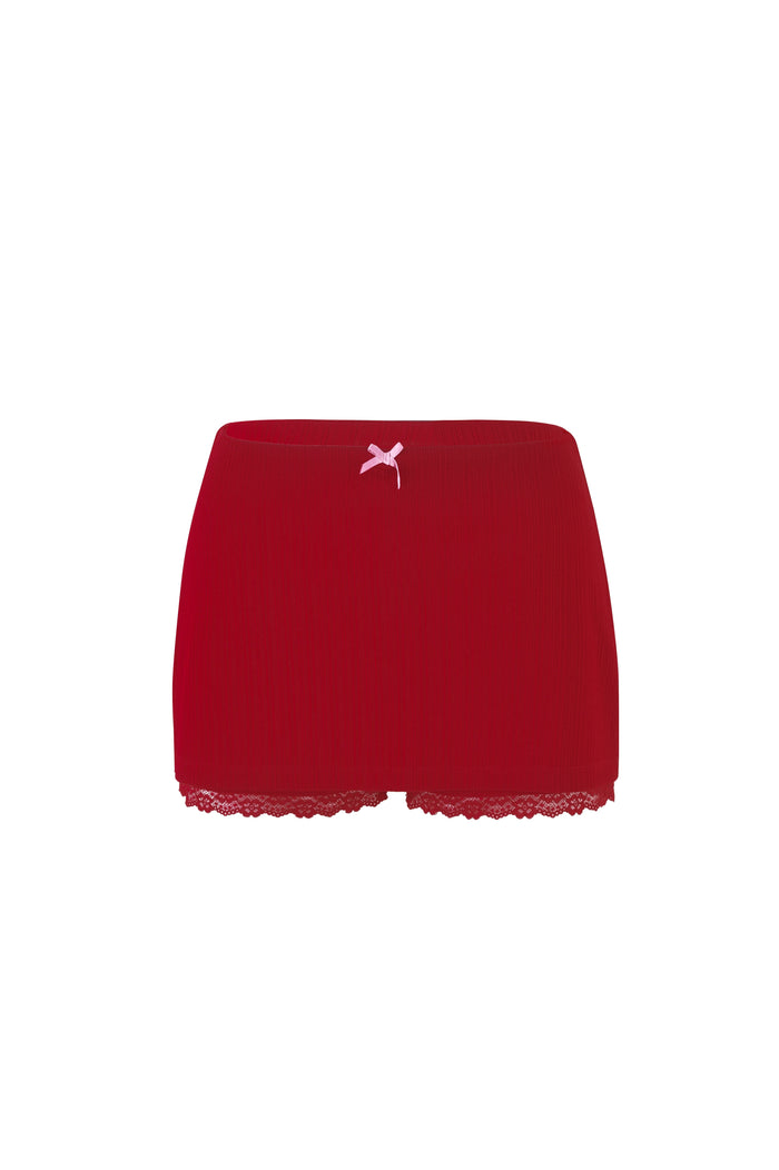 The SABINE SKORT by TIGERMIST in Berry Red and Pink Crimson features a red lace-trimmed design accented with a pink ribbon bow at the center waistband. The ribbed fabric and delicate lace detailing along the hem enhance its elegance. Displayed against a plain white background.