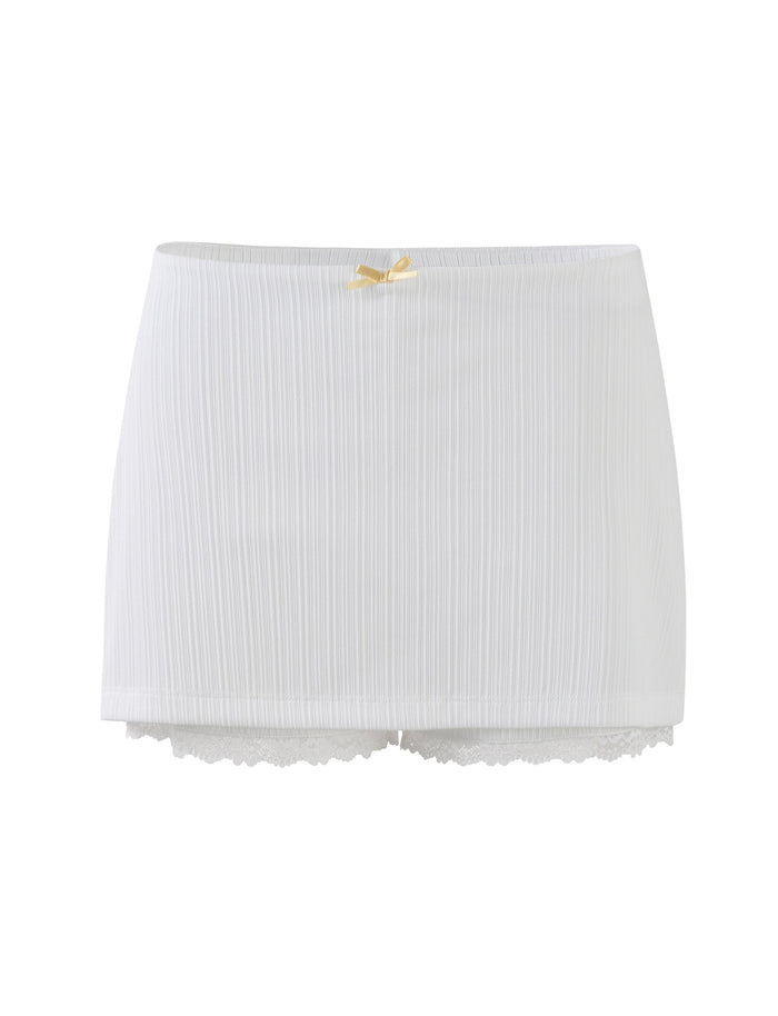 Introducing the SABINE SKORT – WHITE from TIGERMIST: This elegant piece features a ribbed texture and a small yellow bow at the waistband. The bottom edge is adorned with delicate lace trim, and its lightweight material has a slightly sheer quality.
