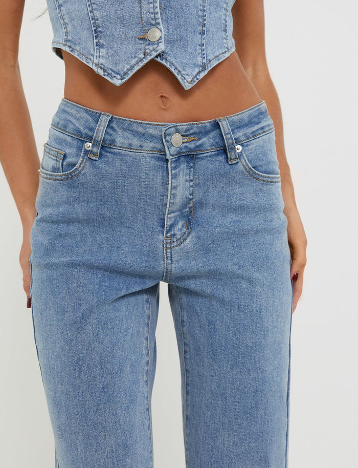 A person wearing TIGERMIST's TATYANA JEANS in light wash blue denim and a matching Tiger Mist denim crop top. The crop top features a pointed hem and silver buttons, while the fitted jeans come with front pockets and belt loops. The photo is cropped to display the torso and lower body.