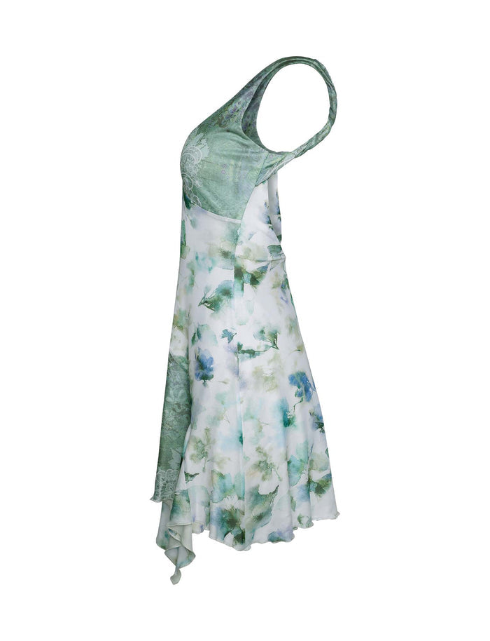 The TIGERMIST THEO DRESS - GREEN : FLORAL is a sleeveless piece with an open back, displaying an elegant green and white floral pattern on a white background. When laid on a white surface, this dress boasts a fitted bodice paired with a flowing skirt that elegantly cascades into an asymmetrical hemline.