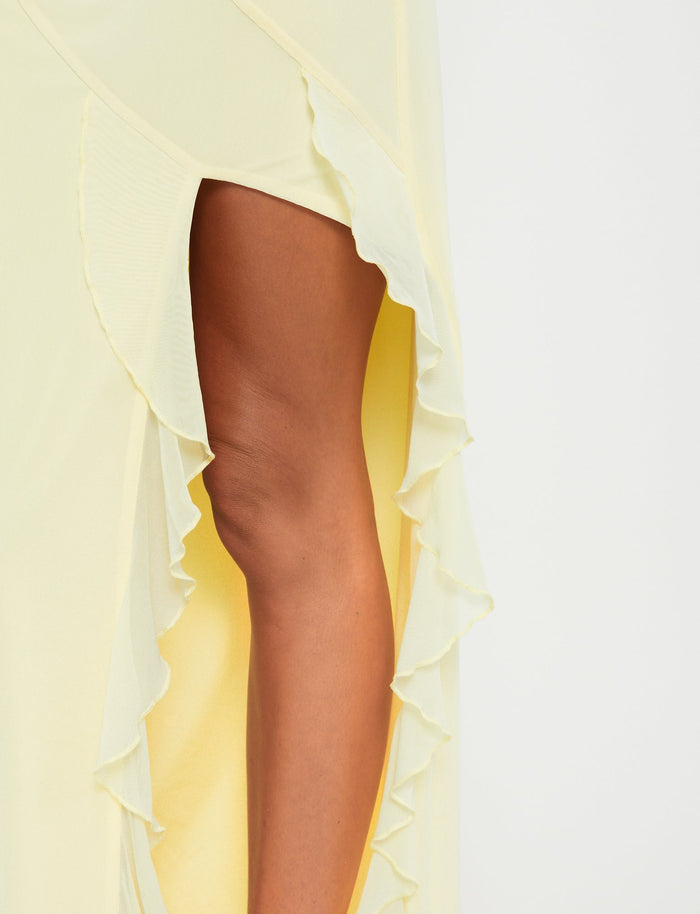 A close-up of the light yellow Theo Skirt - Lemon by TIGERMIST, showcasing its high side slit and ruffled edges. The slit reveals the wearer's leg against a white background.