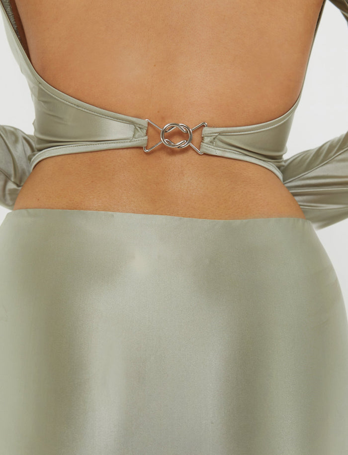 A close-up of a person wearing the THESSALY TOP - GREEN from TIGERMIST. The top features a stunning X-shaped strap design at the open back, fastened by a small silver buckle in the center. The MATCHA GREEN fabric has a smooth, reflective finish that adds an extra touch of elegance.