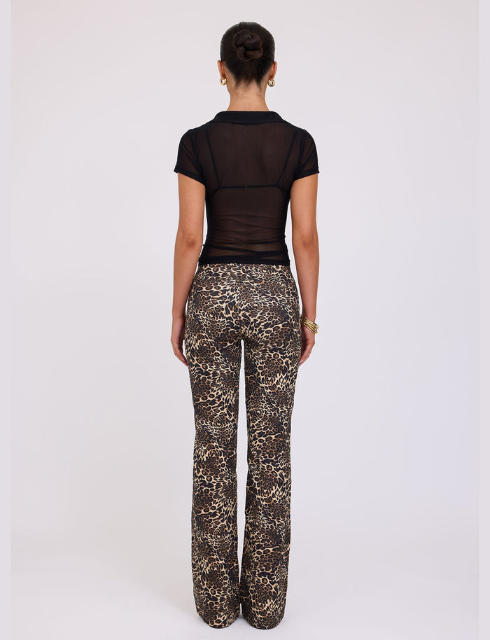 A person with hair in a bun is standing with their back to the camera, sporting a short-sleeve, sheer, black TIGERMIST top and the VESPER PANT - MULTI : LEOPARD by TIGERMIST. The background is plain and light-colored.