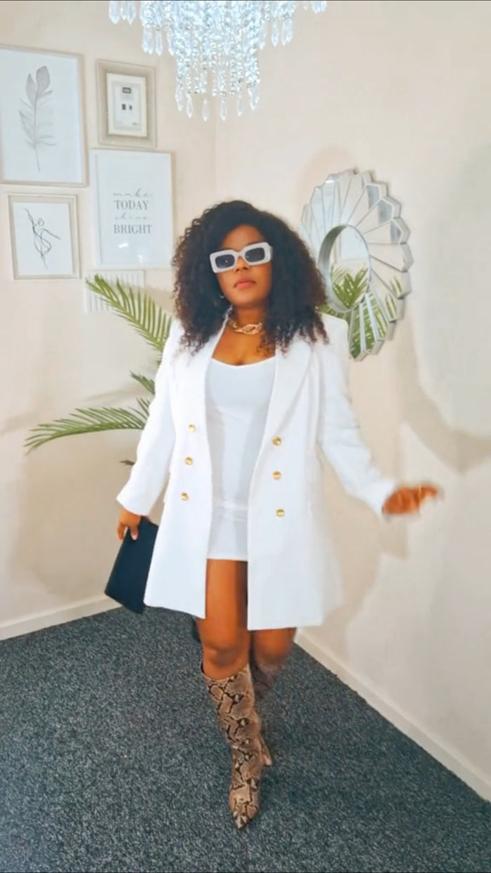 Woman in a white coat and knee-high boots standing in a room with decor elements.