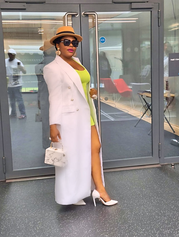 Woman in a structured white statement coat and green top standing in front of glass doors.