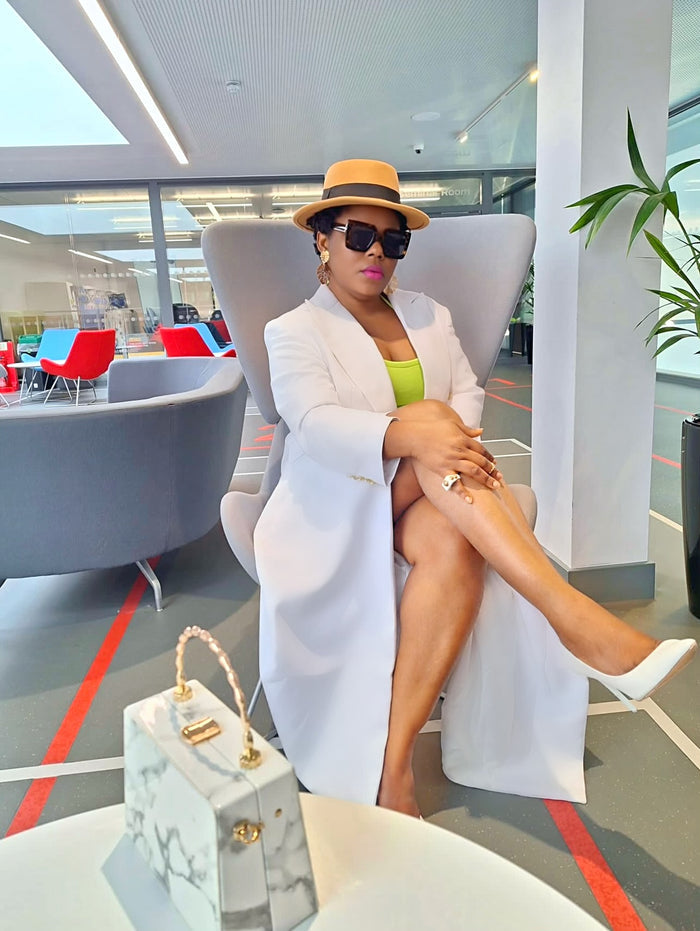 Woman sitting in a modern office setting wearing a white statement coat and sunglasses.